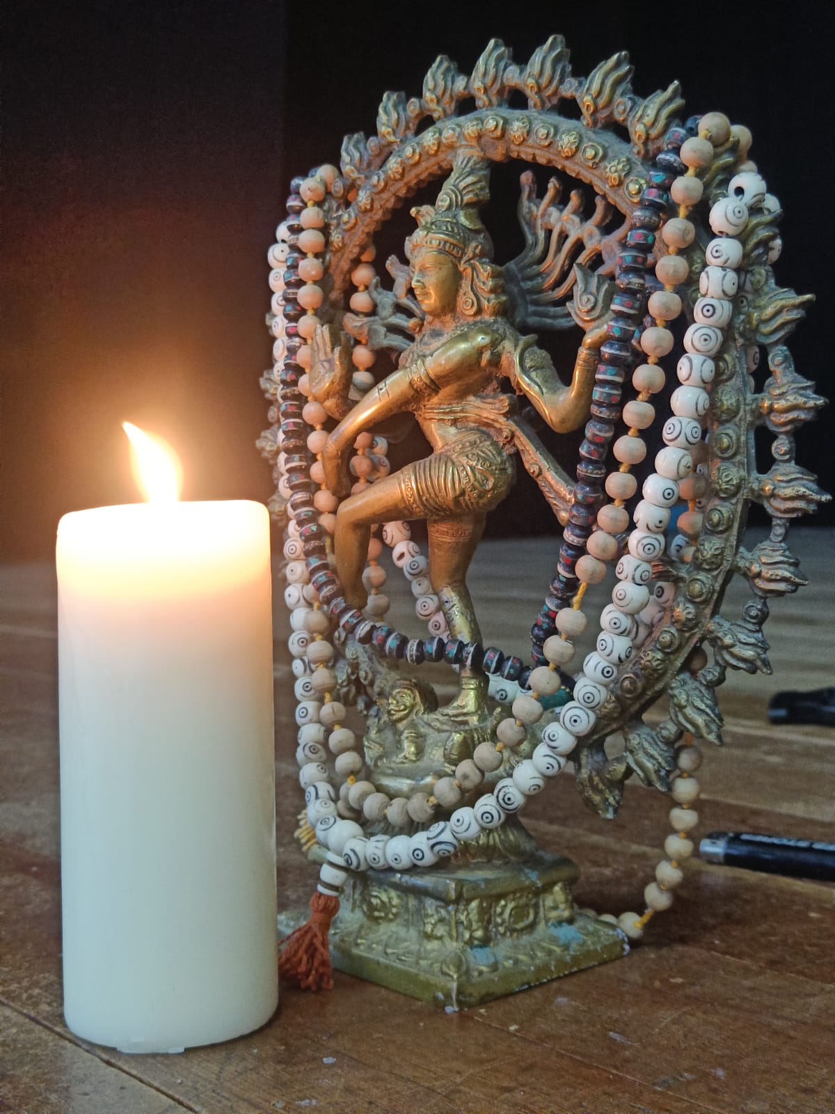 A bronze Nataraj statue of the dancing Shiva beside a lit candle and mala beads