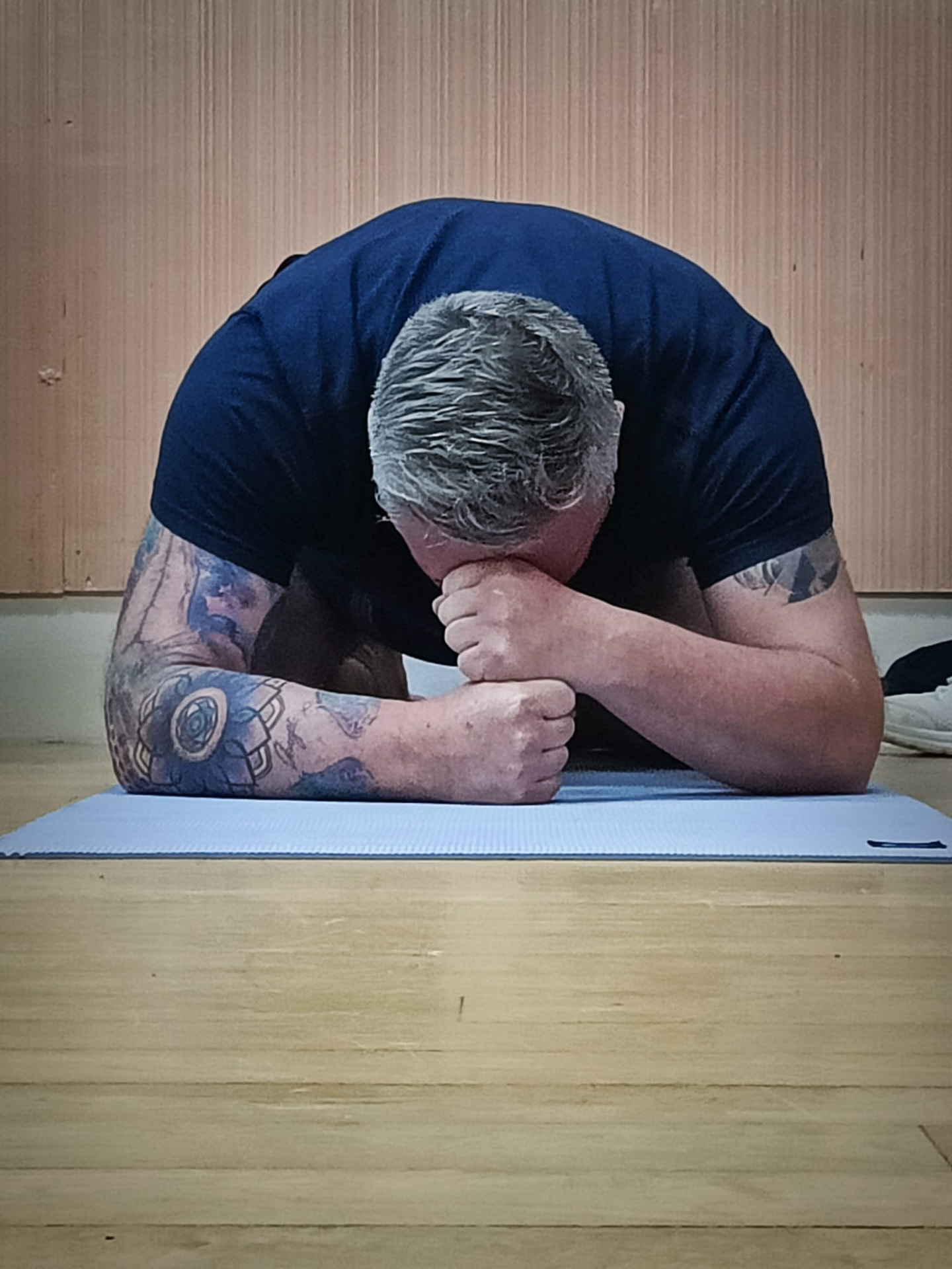 Michael resting in child's pose on a yoga mat in a wood-panelled studio